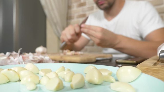 a man peels garlic sitting at a table on a background of a brick wall.