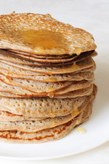 A pile of homemade freshly baked Russian pancakes on the white plate with honey sprinkle flowing from the top