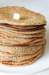 A pile of homemade freshly baked Russian pancakes with a piece of butter on the top on the white plate