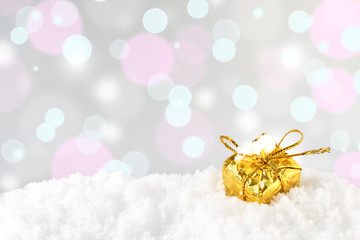 A golden shiny decorative Christmas or New Year gift box with a bow is standing in the snow against the background of twinkling bokeh of lights. Background for greeting card with copy space.