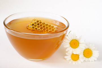 A bowl of fresh organic honey with a piece of honeycomb in it isolated on white