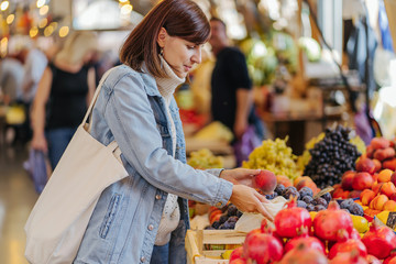 Young Woman puts fruits and vegetables in cotton produce bag at food market. Reusable eco bag for shopping. Sustainable lifestyle. Eco friendly concept.