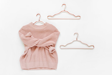 Pale pink knitted sweater with metallic hangers on white background. Autumn and winter clothes....