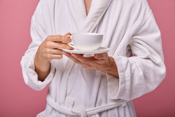 Un sleepy young man in a sleeping mask on his head in a white coat with a with a cup of coffee in...