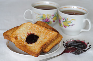 Toasts with black currant jam and two white tea cups in the background