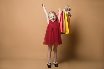 A young girl in a red dress and with shopping bags, very happy shopping. A young girl stands on an orange background
