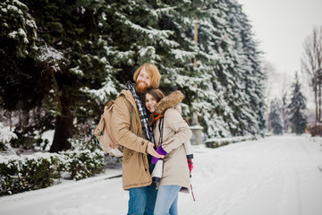 Fototapeta na wymiar Beautiful young Caucasian people couple lovers on a date in winter park. A guy with a beard, skates and a backpack hugs, a man loves a woman a date Valentine's Day in nature