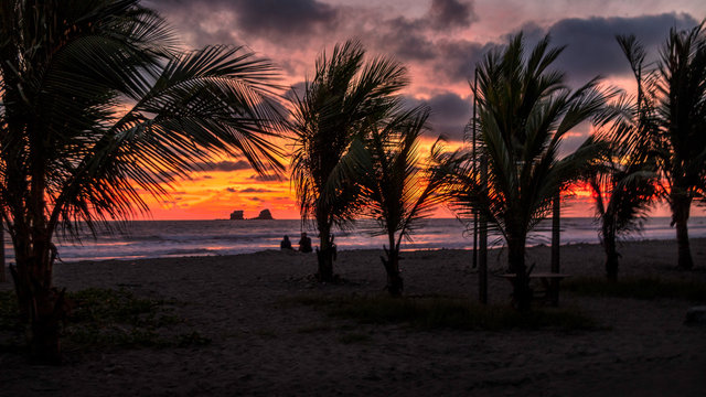 Amazing sunset at the beach. Ocean waves, palm trees, sand and a island can be seen. Latin America