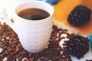 Cup of coffee with scattered coffee beans, pine cone on white background. Autumn morning mood, copy space.
