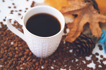 Cup of coffee with scattered coffee beans, dry yellow leaves on white table. Autumn morning mood, copy space.