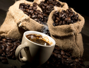 Coffee cup and sacks with coffee beans on a black table.