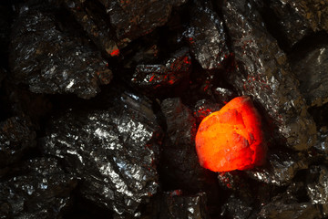 Red hot coal bar in focus on other cold raw bars of coal. Background of raw coal nuggets  with soft...