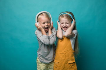 Very emotional children listen to music with headphones on a blue background. Boy and girl are dancing and showing different emotions and he is happy