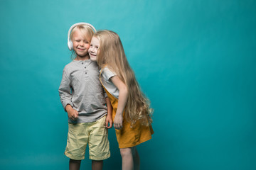 Very emotional children listen to music with headphones on a blue background. Boy and girl are dancing and showing different emotions and he is happy
