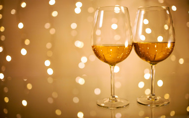 Pair of wine glasses on glass table against golden bokeh lights background, festive and fun concept 