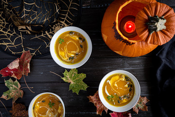 Fototapeta na wymiar Halloween pumpkin soup and carrot soup with cream, parsley and pumpkin seeds on dark wooden background