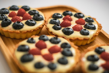 Homemade berry cakes with raspberries and blueberries on bamboo tray