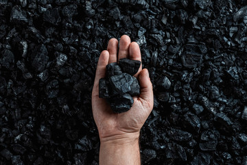 Male hand with coal on the background of a heap of coal, coal mining in an open pit quarry, copy...
