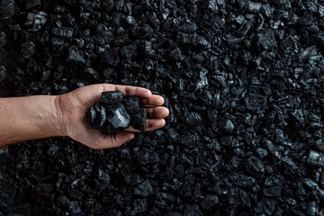 Male hand with coal on the background of a heap of coal, coal mining in an open pit quarry, copy...
