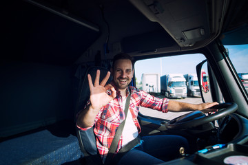 Truck driver loving his job and showing okay gesture sign while sitting in his truck cabin....