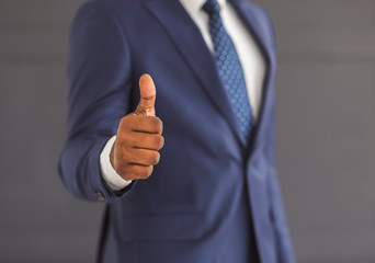 Unrecognizable businessman showing thumb up gesture over grey background