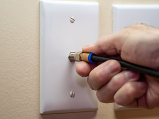 Male electrician connecting coax cable cord to wall outlet. Coaxial wire connection for TV and high...