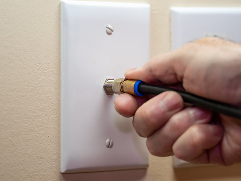 Male electrician connecting coax cable cord to wall outlet. Coaxial wire connection for TV and high speed broadband internet. Television service installation.