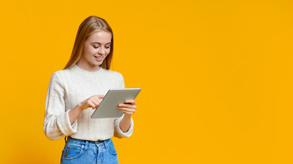 Beautiful teen girl using digital tablet over orange studio background