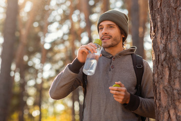 Young tourist with backpack drinking water, having break