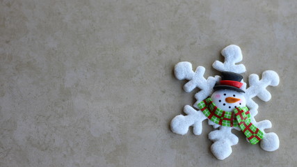 white snowflake decorated with a snowman face in the center wearing a hat and scarf close up on a tan background with copy space