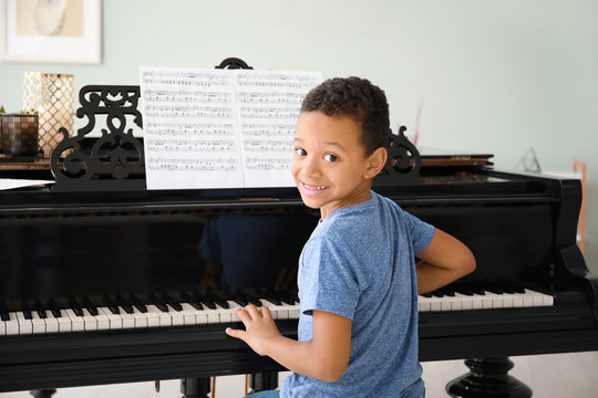 Little African-American boy playing grand piano at home - Powered by Adobe