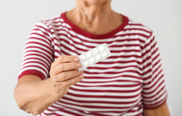 Elderly woman with pills on light background