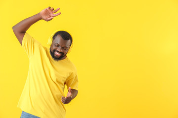 Handsome African-American man listening to music and dancing against color background