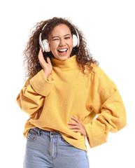 Beautiful African-American woman listening to music on white background