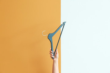 Female hand with clothes hanger on color background