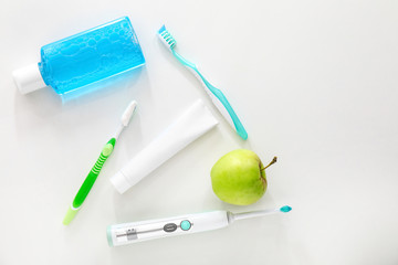 Different tooth brushes with mouth rinse, paste and apple on white background