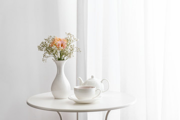 Fototapeta na wymiar Vase with beautiful flowers and tea on table in room
