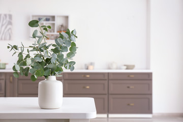 Vase with eucalyptus branches on table in kitchen