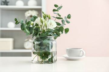 Vase with beautiful flowers and cup of tea on table in room