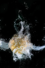 Sphère dorée plongeant dans l'eau, sur fond noir