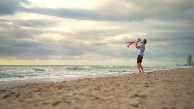 little beautiful baby girl plays with father infront of sea