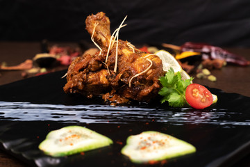 Spicy chicken legs in a dry curry in a skillet on a black slate, stone or concrete background garnished with tomato and coriander lief. Top view with copy space.