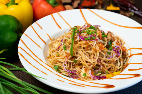 Vegetarian Schezwan Noodles or Vegetable Hakka Noodles or Chow mein in white bowl at dark background and garnished with fresh Vegetables and Indian spices. Fast food concept with Copy space.