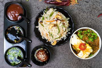 Mix Indian food with Long grain fried rice and chicken curry or egg curry served with sauces and Gulab jamun in sweets, Decorated with Indian spices on wooden background