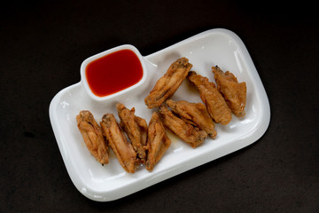 Served fried chicken wings with dipping sauce on a set of white tiles placed on a black background.
