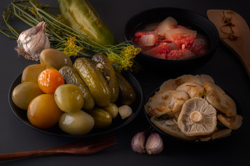 Fermented products cabbage, peppers, pickles, tomatoes, mushrooms, zucchini, garlic on a dark table. Low key
