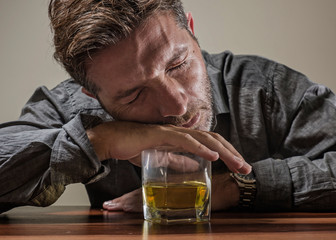alcoholic depressed and drunk addict man sitting in front of whiskey glass trying holding on drinking in dramatic expression suffering alcoholism and alcohol addiction