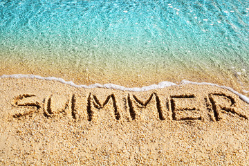 Word SUMMER written on yellow sand, blue sea wave, white foam top view close up, handwriting...