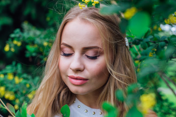 Fototapeta premium Close up portrait of a charming blond woman wearing beautiful white dress standing next to barberry bush.