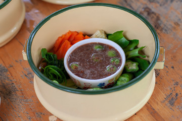 Shrimp Paste Chili Sauce and Vegetable in yellow vintage metal food carrier or tiffin carrier on wooden table.
